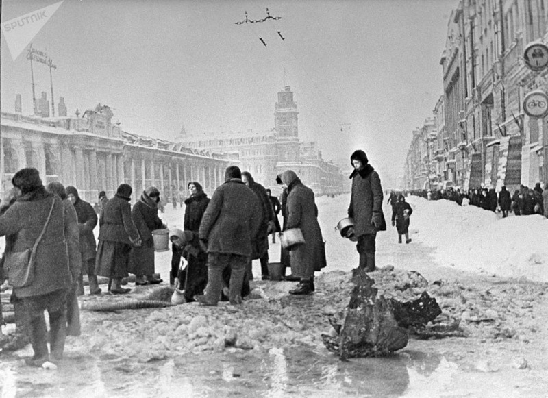 Жители блокадного Ленинграда набирают воду, появившуюся после артобстрела в пробоинах в асфальте.